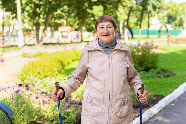 An elderly woman walks nordic with sticks in the park on a sunny summer day