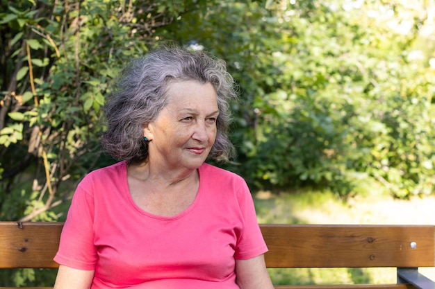 Elderly woman with gray hair in the park. Granny with wrinkles and freckles on her face smiling looking to the side