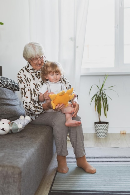 Elderly woman with her little grandson playing at home on the sofa