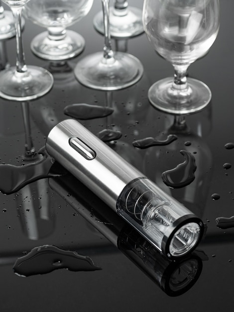 Electric corkscrew in gray metal Lies on a mirrored surface Empty glass goblets in the background