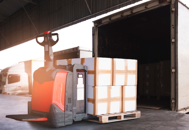 Electric forklift pallet jack with stack of cargo boxes unloading into container truck. Cargo freight shipment by truck.