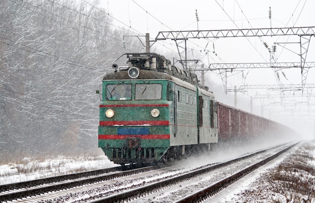 Electric freight train is moving in a snowstorm