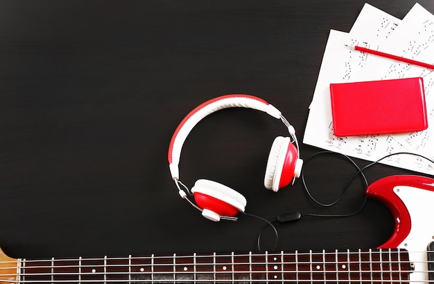 Electric guitar with headphones and notes on black wooden background