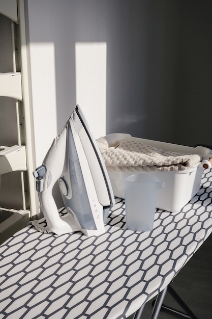 Electric iron and a pile of  beige towels on ironing board in laundry room at home