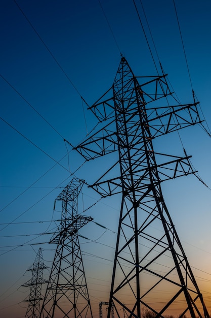 Electric post with wires with sunset background. Transmission tower. Power lines on a colorful sunset. Close up high voltage power lines silhouette. High voltage electric transmission pylon tower.