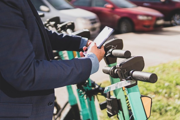 Electric scooter in city Man using smartphone to rent an e kick vehicle guy with mobile phone using eco transport in downtown Business person in traffic Modern urban lifestyle in summer