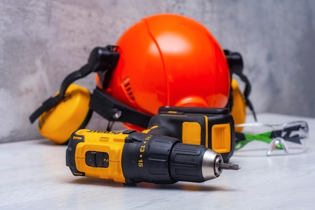 Electric screwdriver and a construction safety helmet for a head with an earpiece and a headlamp on the table Construction tool and form for protection