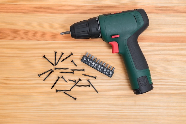 An electric screwdriver lies on a wooden table and various attachments for a cartridge lie near it