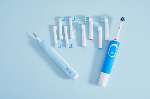 Electric toothbrush and a lot of different multicolored replaceable nozzles on blue background top view copy space