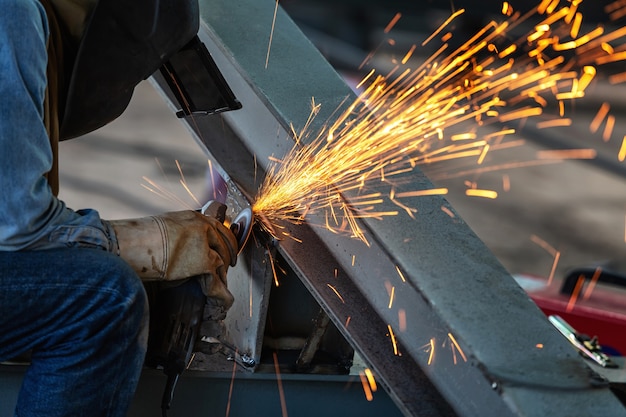 Electric wheel grinding on steel structure and welders with multiple sparks in factory.