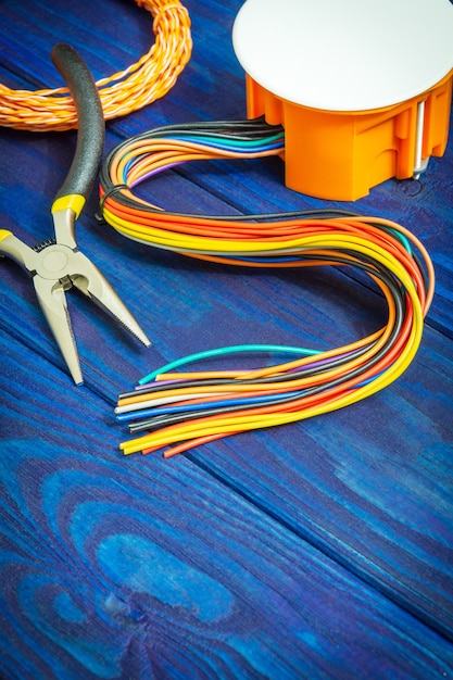 Electrical junction orange box with wires and tool on blue wooden boards usually used in the electric installation process