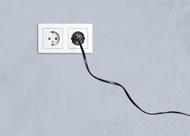 Electrical socket and plug in it against the background of a gray wall