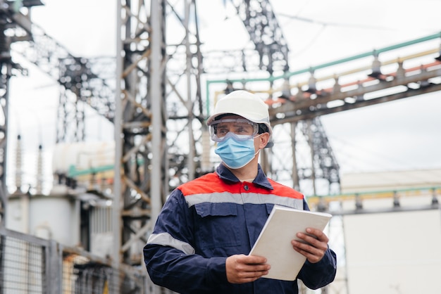 An electrical substation engineer inspects modern high-voltage equipment in a mask at the time of pondemia. Energy. Industry.