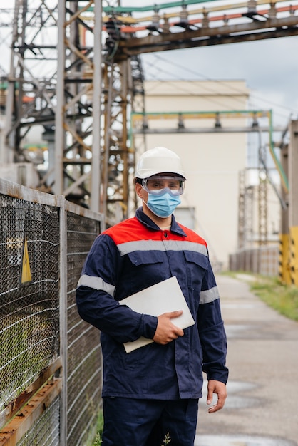 An electrical substation engineer inspects modern high-voltage equipment in a mask at the time of pondemia. Energy. Industry.