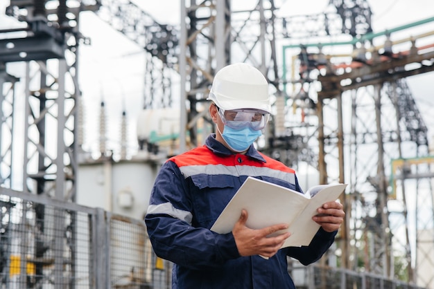 An electrical substation engineer inspects modern high-voltage equipment in a mask at the time of pondemia. Energy. Industry.