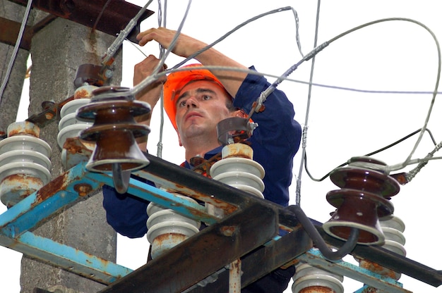 An electrician on an electric pole changes a damaged insulator