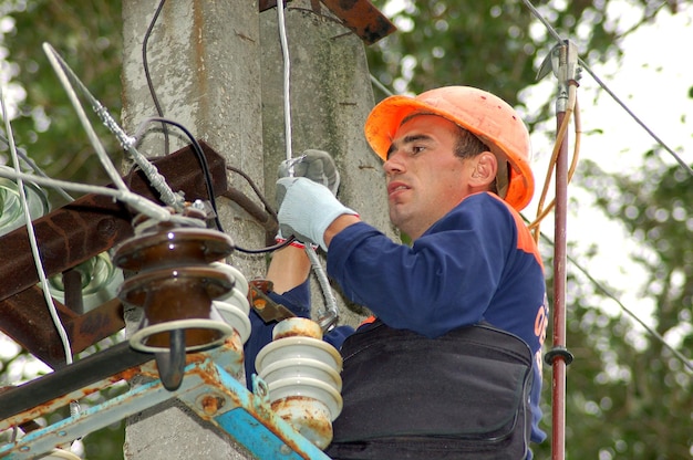 An electrician on an electric pole changes a damaged insulator