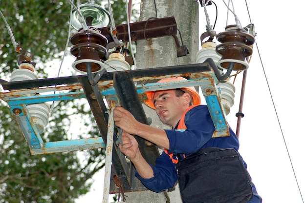 An electrician on an electric pole changes a damaged insulator