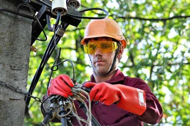 An electrician on an electric pole repairs wires on a power line