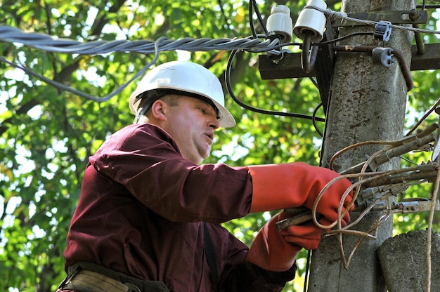 An electrician on an electric pole repairs wires on a power line