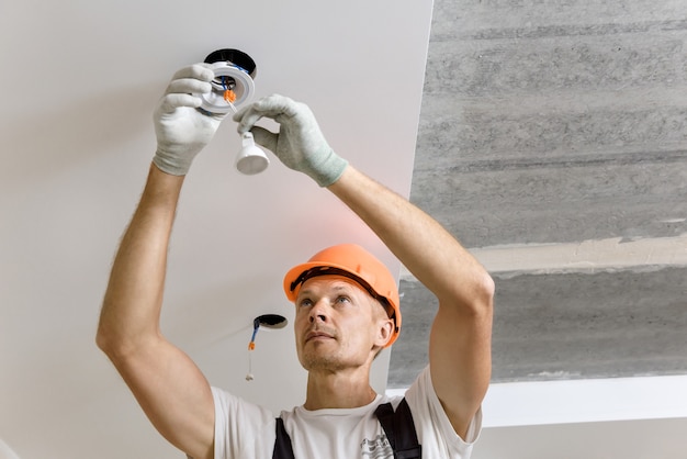 The electrician is installing LED spotlights on the ceiling.