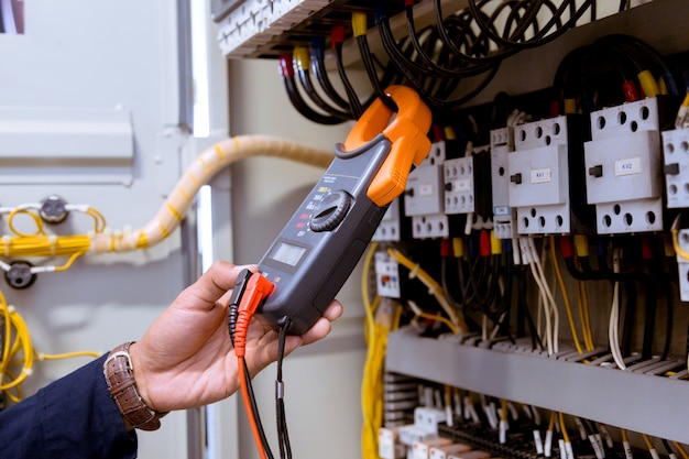 Electrician measurements with multimeter testing current electric in control panel.