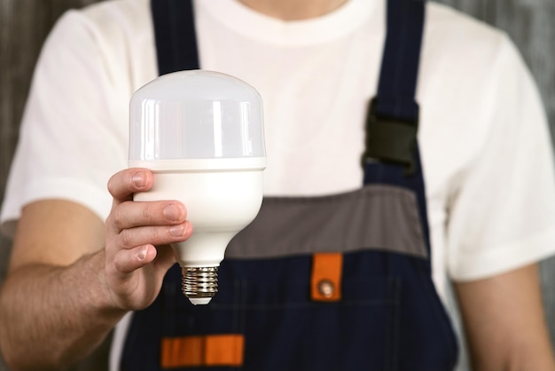 An electrician in overalls holding an energysaving light bulb in his hands