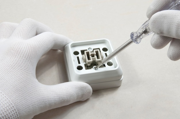 Electrician repairs a light switch on a wall in white gloves