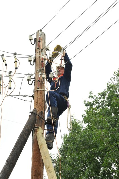 Electrician on a wooden pylon installs the grounding on the power line before repairing it.