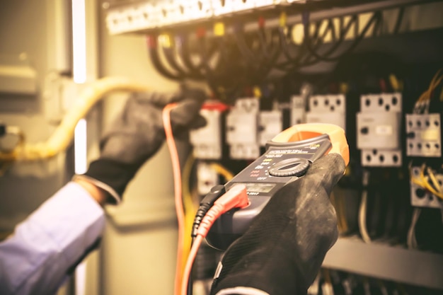 Electricity and electrical maintenance service Engineer using measuring equipment tool checking electric current voltage at circuit breaker terminal and cable wiring main power distribution board