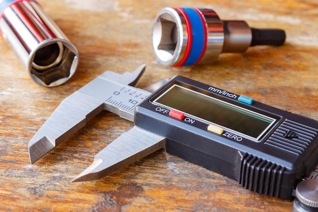 Electronic caliper with spanners heads on wooden table in workshop