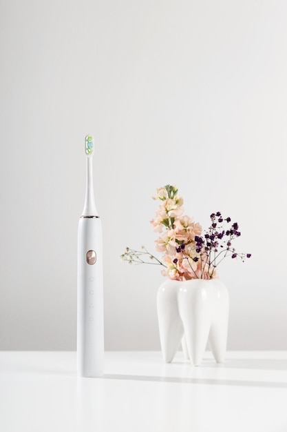 Electronic toothbrush next to decorative model of tooth on white background