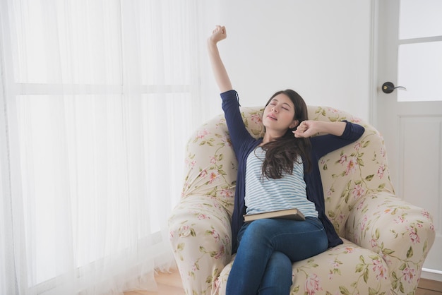 elegance slim girl studying school book sitting in front of window comfortable sofa and feeling tired stretching body on living room at home.