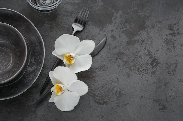 Elegance table setting with knitted grey napkin cutlery ceramic plates glasses and white orchid flowers