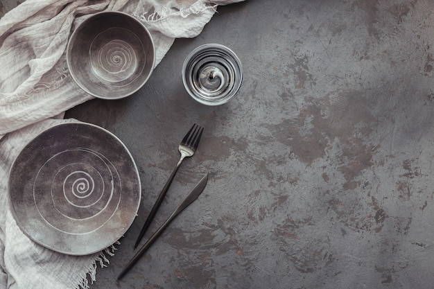 Elegance table setting with knitted grey napkin, cutlery, ceramic platesand glasses on dark table. Holiday modern table decoration. Romantic dinner.