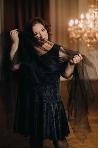 An elegant adult woman in a black cocktail dress poses in the interior Fashionable portrait of a woman