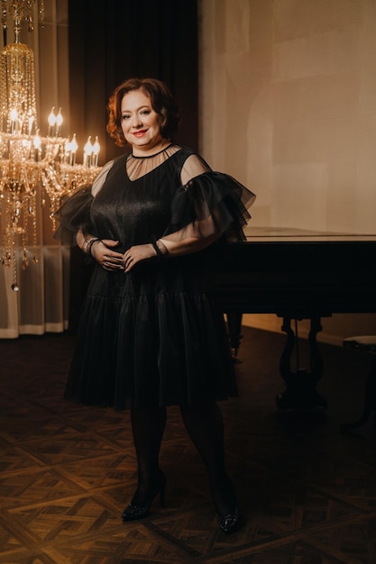 An elegant adult woman in a black cocktail dress poses in the interior Fashionable portrait of a woman