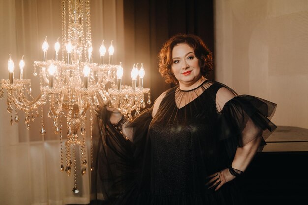 An elegant adult woman in a black cocktail dress poses in the interior Fashionable portrait of a woman