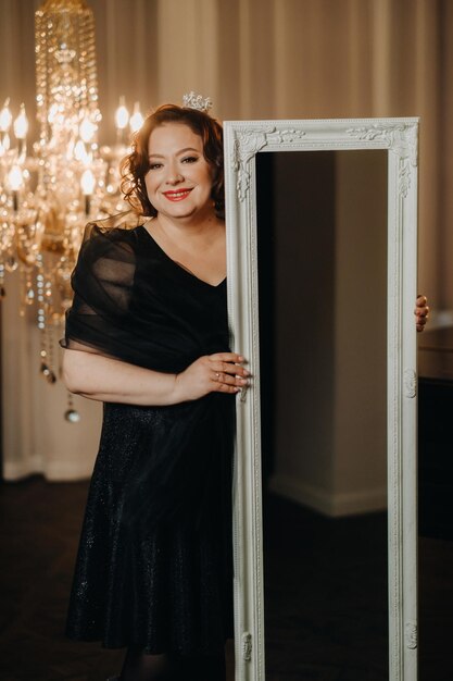 An elegant adult woman in a black cocktail dress poses in the interior Fashionable portrait of a woman