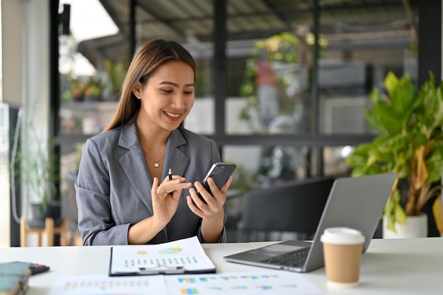 Elegant Asian businesswoman using her smartphone at her desk text chat message