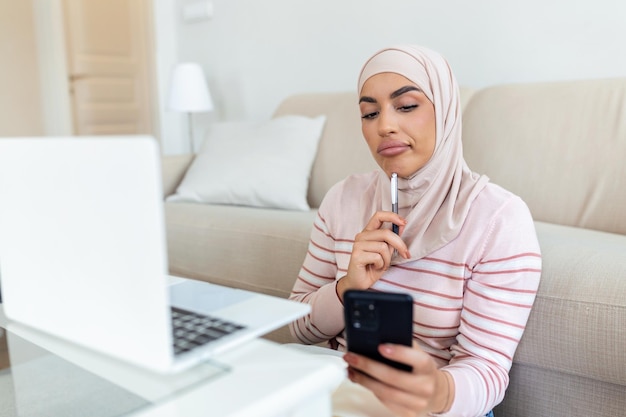 Elegant attractive Muslim woman using mobilephone and laptop searching online shopping information in living room at home Portrait of happy woman purchasing product via online shopping