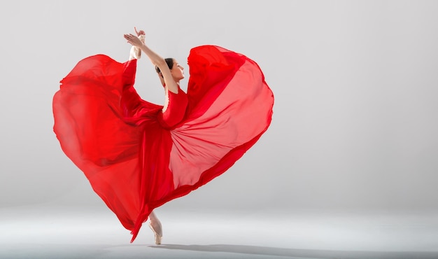 Elegant ballerina in pointe shoes dancing in a long red skirt developing in the shape of a heart on a white background