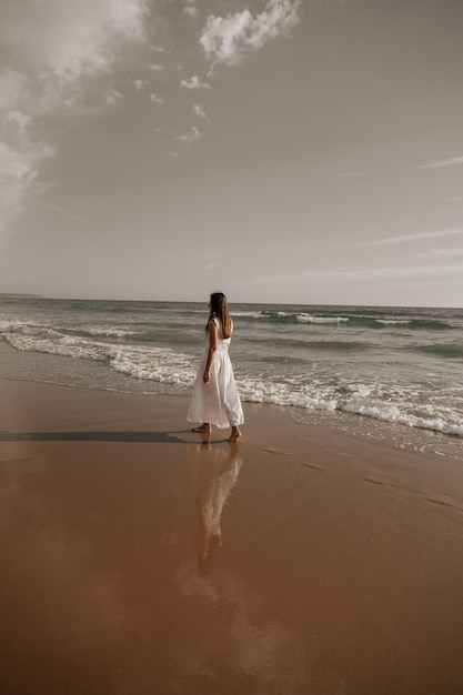 Elegant barefooted female tourist walking near foamy ocean