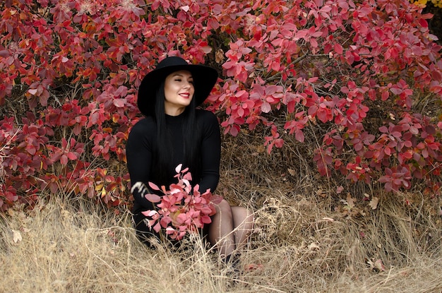 Elegant beautiful brunette woman sitting in an autumn park with a bouquet of red leaves in her hands