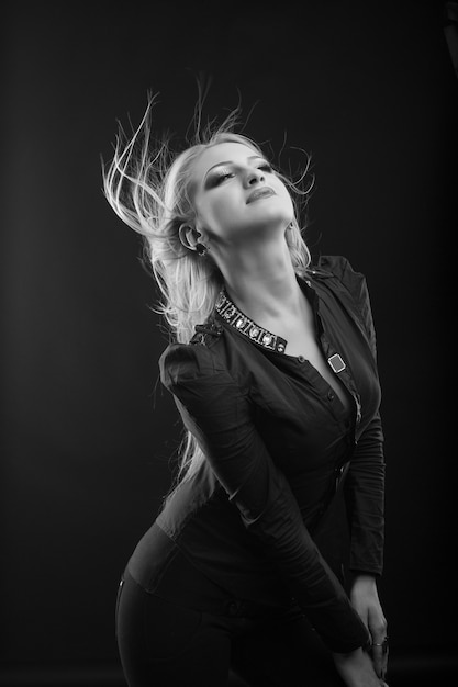 Elegant blond woman with perfect makeup and long fluttering hair wears blouse, posing at studio. Black and white shot