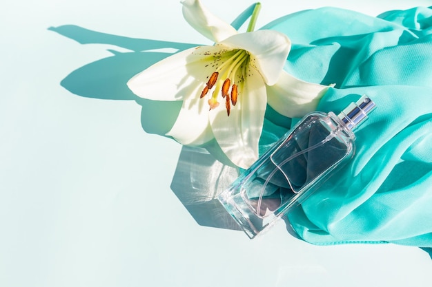 An elegant bottle of cosmetic spray or perfume against the background of a light scarf and a white lily flower space for text aroma presentation