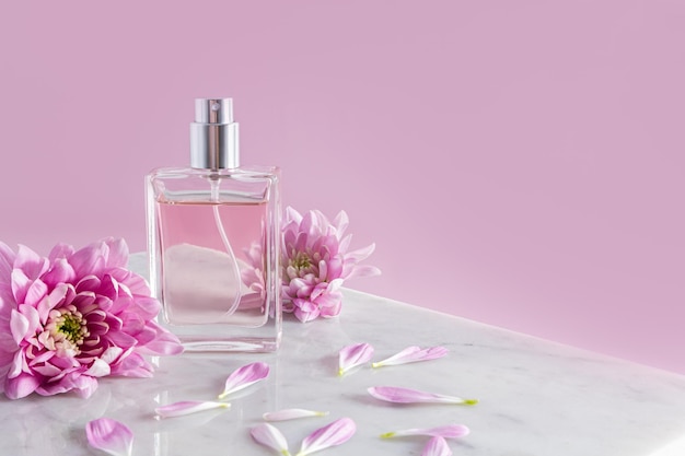 An elegant bottle of cosmetic spray stands on part of a white marble podium with chrysanthemum flowers pink background a copy space