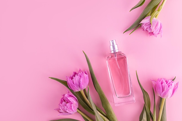 Elegant bottle of pink perfume among tulips on pink background Top view Flat lay A copy space Presentation of a fragrance Blank bottle mockup