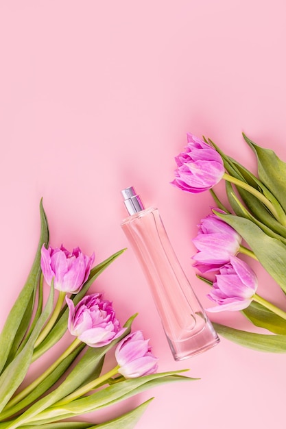 Elegant bottle of pink perfume among tulips on pink background Top view Flat lay Presentation of a fragrance Blank bottle mockup Vertical view