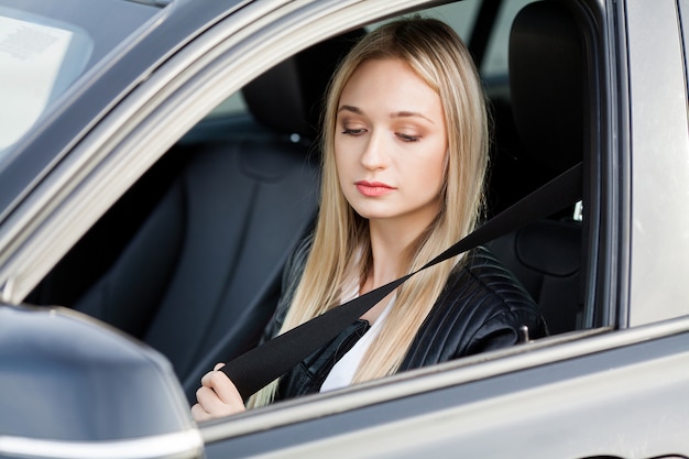 Elegant business woman dressed in the suit fastening the safe belt before driving his car